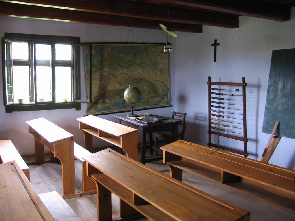 Ilustración en acuarela de un aula tradicional con bancos de madera, globo terráqueo, mapa mural, ábaco y pequeña cruz, en tonos tierra cálidos y atmósfera serena